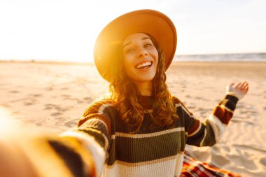 Selfie zamanı. Gün batımında deniz kenarında poz veren genç bir kadın. Seyahat, yaşam tarzı, moda, blog yazma.