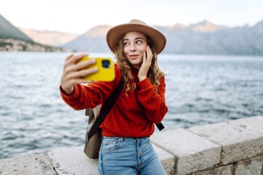 Sonbahar kıyafetleri içinde mutlu bir kadın dışarıda akıllı telefondan selfie çekiyor. Telefonu olan şık bir kadın. Tatil kavramı, teknoloji, hafta sonu.