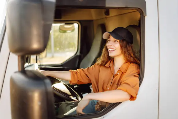 Portrait of beautiful young woman professional truck driver  driving a big truck. Inside of vehicle. People and industrial transportation concept.