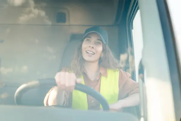 Portrait of beautiful young woman professional truck driver  driving a big truck. Inside of vehicle. People and industrial transportation concept.