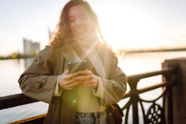 Sonbahar kıyafetleri içinde, setin üzerinde telefonu olan mutlu bir kadın. Telefonu olan şık bir kadın. Tatil kavramı, teknoloji, hafta sonu.