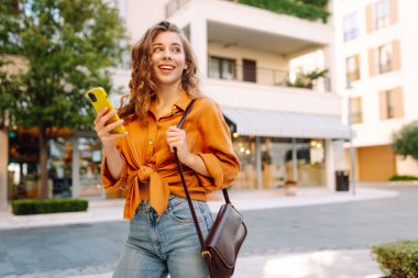 Sokakta yürürken telefonu olan güzel bir kadın. Yaşam tarzı, seyahat, turizm, teknoloji, blog yazma, iletişim kavramı.