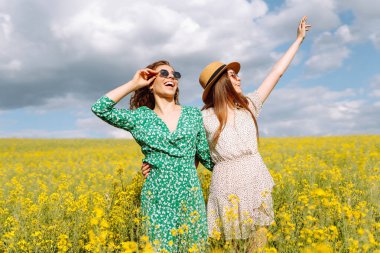 Sarı çiçekli güzel bir tarlada iki genç kadın. Zıplarlar ve eğlenirler. Dostluk Günü