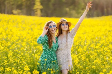 Sarı çiçekli güzel bir tarlada iki genç kadın. Zıplarlar ve eğlenirler. Dostluk Günü