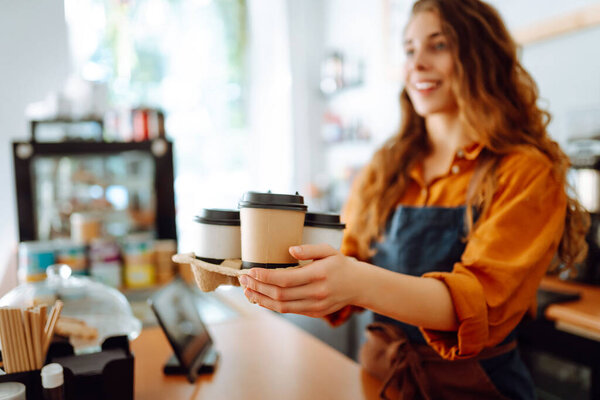 Portrait of a young woman barista holding takeaway coffee in her hands. Takeaway food. Business concept.