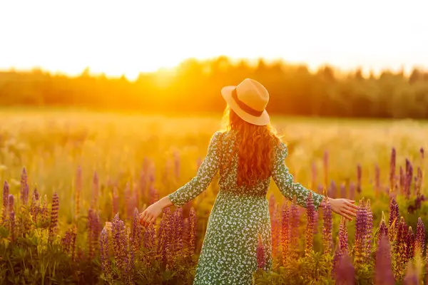 Beautiful woman stands on blooming fragrant lavender fields, collects flowers, inhales fresh floral air.  Nature, vacation, relax and lifestyle.