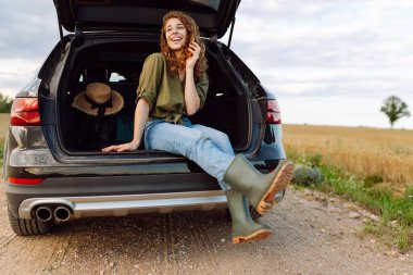Bagajda oturan genç bir kadın, dinleniyor ve yolculuğun tadını çıkarıyor. Yaşam tarzı, seyahat, turizm, aktif yaşam.