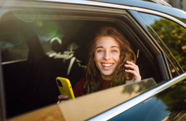 Akıllı telefon kullanan mutlu bir kadın, arabanın arka koltuğunda oturuyor, sosyal medya haberlerini sarıyorum, e-posta mektuplarını okuyorum, arkadaşlarla iletişim kuruyorum, mesajlar alıyorum, online alışveriş yapıyorum..