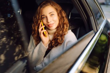 Akıllı telefon kullanan mutlu bir kadın, arabanın arka koltuğunda oturuyor, sosyal medya haberlerini sarıyorum, e-posta mektuplarını okuyorum, arkadaşlarla iletişim kuruyorum, mesajlar alıyorum, online alışveriş yapıyorum..