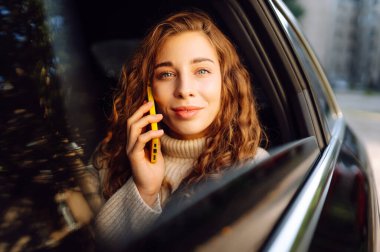 Akıllı telefon kullanan mutlu bir kadın, arabanın arka koltuğunda oturuyor, sosyal medya haberlerini sarıyorum, e-posta mektuplarını okuyorum, arkadaşlarla iletişim kuruyorum, mesajlar alıyorum, online alışveriş yapıyorum..