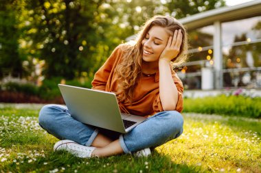 Yeşil çimlerin üzerinde dizüstü bilgisayarı olan genç kıvırcık kadın. Eğitim çevrimiçi. Bilgi işlem. İş, blog yazma, serbest çalışma kavramı.