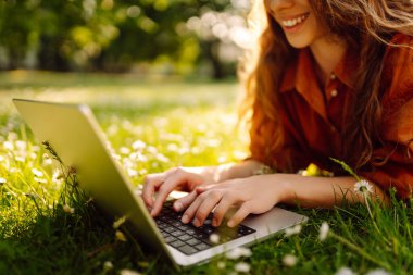 Yeşil çimlerin üzerinde dizüstü bilgisayarı olan genç kıvırcık kadın. Eğitim çevrimiçi. Bilgi işlem. İş, blog yazma, serbest çalışma kavramı.