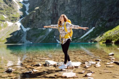Sarı bir sırt çantasıyla dağlarda orman ve kayalıkların arasında yürüyüş parkurları boyunca seyahat eden genç bir kadın. Yaşam tarzı, macera, doğa, aktif yaşam.