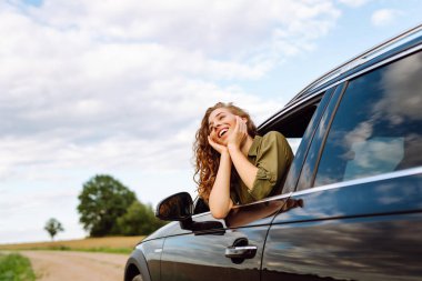 Mutlu kadın dinleniyor ve araba penceresinden dışarı çıkmanın tadını çıkarıyor. Özgürlük, dinlenme, rahatlama. Araba yolculuğu.