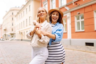 Sokakta yürürken el ele tutuşan neşeli genç bayanlar. Dişi turistler güneşli bir günde şehri gezmenin keyfini çıkarıyorlar. Yaşam tarzı, moda, seyahat kavramı.