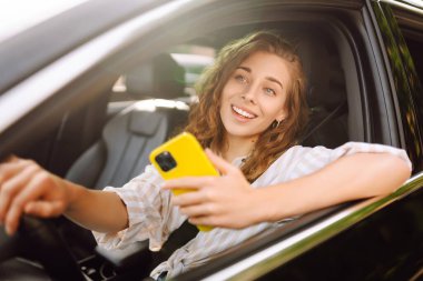 Genç bir kadının portresi telefonla araba sürüyor. Boş zaman, seyahat, teknoloji, navigasyon.