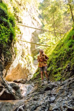Sarı sırt çantalı maceraperest kadın dağ manzarasının arka planında yürüyüş parkurunda yürüyor. Doğa, aktif yaşam.