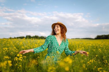 Genç bir kadın sarı çiçeklerle dolu bir tarlada yürüyor. Moda, yaşam tarzı, seyahat ve tatil kavramı.