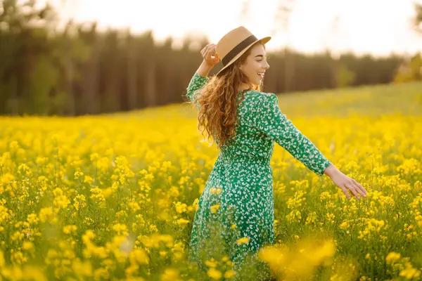 Genç bir kadın sarı çiçeklerle dolu bir tarlada yürüyor. Moda, yaşam tarzı, seyahat ve tatil kavramı.