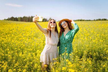Seyahat ederken selfie. Çiçek tarlasında yürürken iki kadın selfie çeker. Moda, güzellik konsepti. 