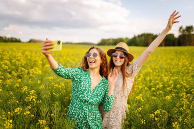 Seyahat ederken selfie. Çiçek tarlasında yürürken iki kadın selfie çeker. Moda, güzellik konsepti. 