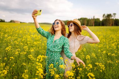 Seyahat ederken selfie. Çiçek tarlasında yürürken iki kadın selfie çeker. Moda, güzellik konsepti. 