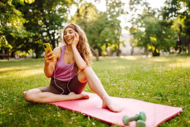 Gelişim, performans ve sağlıklı bir yaşam tarzı için iletişim için akıllı telefonu olan genç bir bayan sporcu. Spor, aktif yaşam, sağlıklı yaşam tarzı.