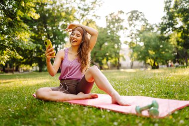 Gelişim, performans ve sağlıklı bir yaşam tarzı için iletişim için akıllı telefonu olan genç bir bayan sporcu. Spor, aktif yaşam, sağlıklı yaşam tarzı.