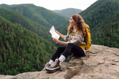 Sırt çantalı kadın turist dağda elinde kağıt haritayla oturuyor. Seyahat, tatil, macera konsepti.