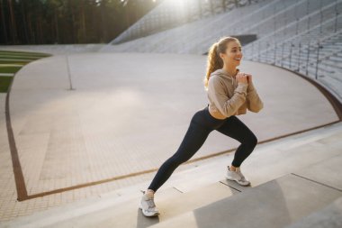 Açık havada sabah jimnastiği yapan gülümseyen genç bir kadın. Aktif hayat, spor eğitimi, sağlıklı yaşam tarzı.