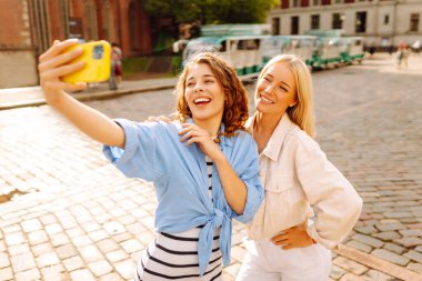 Sokakta yürürken selfie çeken mutlu kadınlar. Moda, seyahat, teknoloji, blog konsepti.