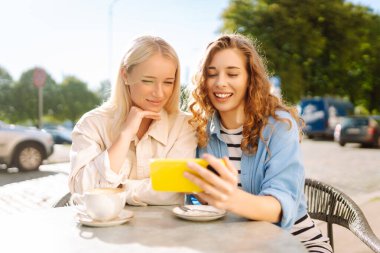 İki genç kadın kafede oturmuş, kahvelerini yudumluyor ve akıllı telefonlarıyla eğleniyorlar. Alışverişten sonra kahve molası. Moda, güzellik, blog, turizm.