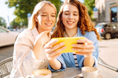İki genç kadın kafede oturmuş, kahvelerini yudumluyor ve akıllı telefonlarıyla eğleniyorlar. Alışverişten sonra kahve molası. Moda, güzellik, blog, turizm.