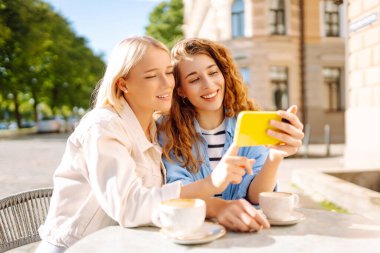 İki genç kadın kafede oturmuş, kahvelerini yudumluyor ve akıllı telefonlarıyla eğleniyorlar. Alışverişten sonra kahve molası. Moda, güzellik, blog, turizm.