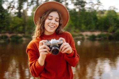 Şapkalı ve sıcak sonbahar elbiseli bir kadın. Aynalı film kamerasıyla doğal olarak poz veriyor. Seyahat blogu. Macera, tatil konsepti.