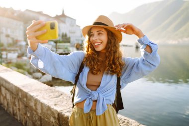 Güzel bir turist sokakta yürüyüp akıllı telefon kamerasıyla selfie çekiyor. Yaşam tarzı, seyahat, dinlenme, hafta sonu, aktif yaşam.