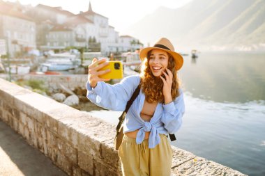 Güzel bir turist sokakta yürüyüp akıllı telefon kamerasıyla selfie çekiyor. Yaşam tarzı, seyahat, dinlenme, hafta sonu, aktif yaşam.