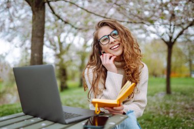Parkta oturup dizüstü bilgisayar kullanan güzel bir kadın. Eğitim çevrimiçi. Bilgi işlem. İş, blog yazma, serbest çalışma kavramı.