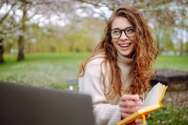 Parkta oturup dizüstü bilgisayar kullanan güzel bir kadın. Eğitim çevrimiçi. Bilgi işlem. İş, blog yazma, serbest çalışma kavramı.