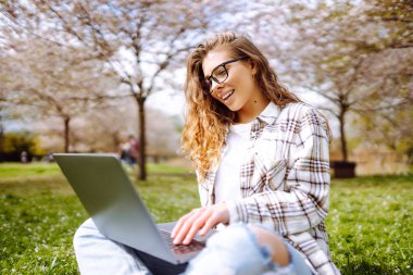 Parkta oturup dizüstü bilgisayar kullanan güzel bir kadın. Eğitim çevrimiçi. Bilgi işlem. İş, blog yazma, serbest çalışma kavramı.