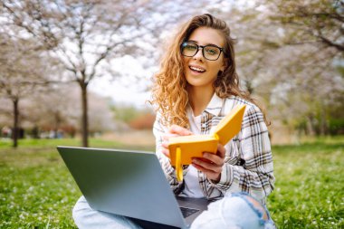 Parkta oturup dizüstü bilgisayar kullanan güzel bir kadın. Eğitim çevrimiçi. Bilgi işlem. İş, blog yazma, serbest çalışma kavramı.