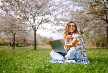 Parkta oturup dizüstü bilgisayar kullanan güzel bir kadın. Eğitim çevrimiçi. Bilgi işlem. İş, blog yazma, serbest çalışma kavramı.