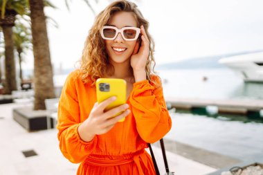 Sokakta yürüyen ve cep telefonu kullanan genç bir kadın. Seyahat, moda, iletişim, blog konsepti. 