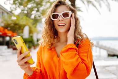 Sokakta yürüyen ve cep telefonu kullanan genç bir kadın. Seyahat, moda, iletişim, blog konsepti. 