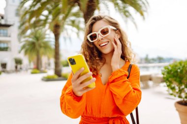 Sokakta yürüyen ve cep telefonu kullanan genç bir kadın. Seyahat, moda, iletişim, blog konsepti. 