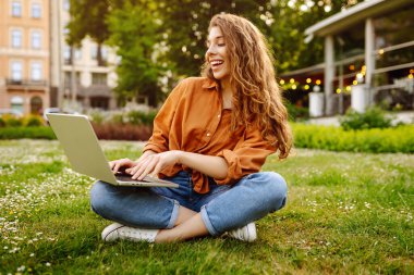 Dışarıda dizüstü bilgisayarı olan kıvırcık saçlı mutlu bir kadın. Çevrimiçi eğitim, Serbest çalışma, teknoloji kavramı.