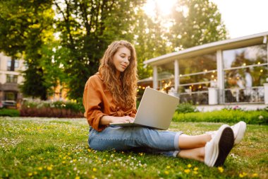 Dışarıda dizüstü bilgisayarı olan kıvırcık saçlı mutlu bir kadın. Çevrimiçi eğitim, Serbest çalışma, teknoloji kavramı.