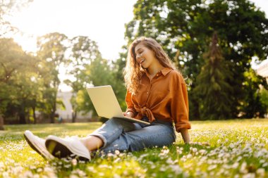 Dışarıda dizüstü bilgisayarı olan kıvırcık saçlı mutlu bir kadın. Çevrimiçi eğitim, Serbest çalışma, teknoloji kavramı.