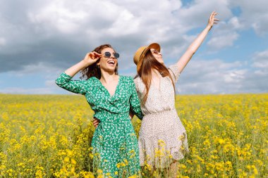 Çiçek açan alanda iki güzel kadın. Moda, tarz kavramı. Aroma ilkbahar doğası sarı çiçek tarlası.
