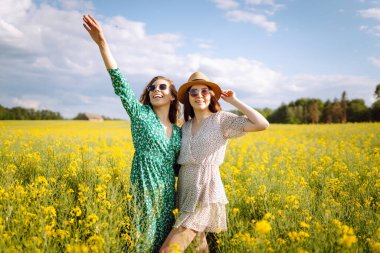 Çiçek açan alanda iki güzel kadın. Moda, tarz kavramı. Aroma ilkbahar doğası sarı çiçek tarlası.